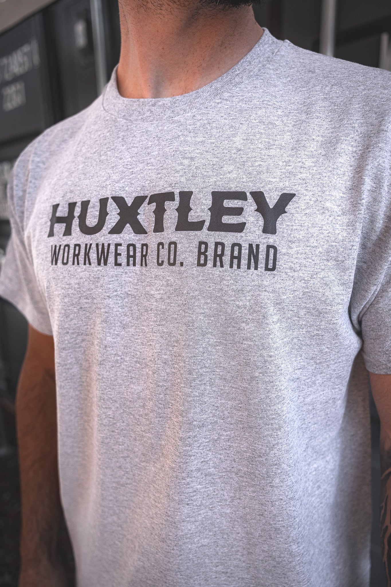 
                  
                    Detailed view of the Huxtley Workwear logo printed across the chest on a heather grey t-shirt. Built tough for everyday wear on site.
                  
                
