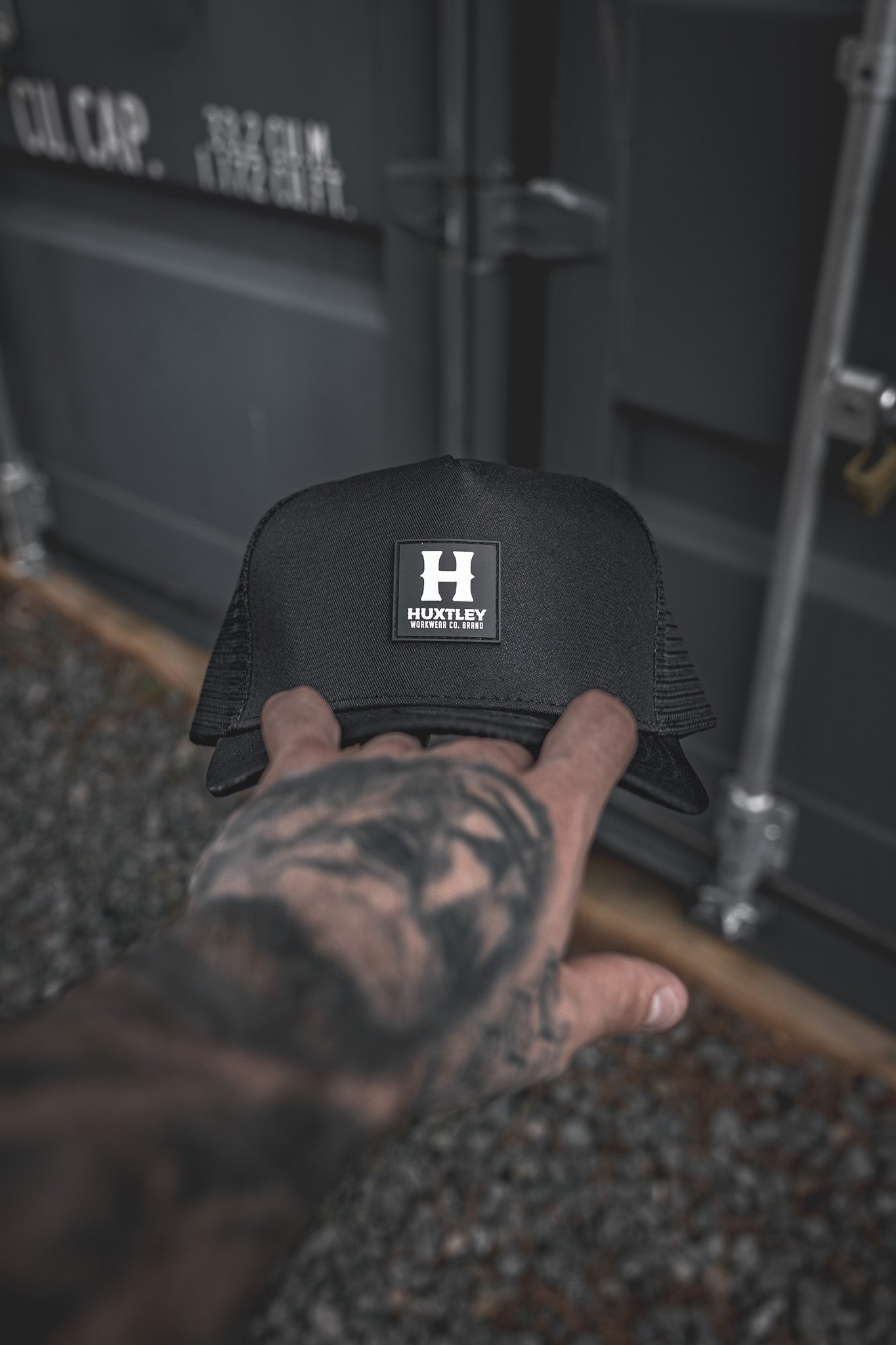 
                  
                    Front view of the Huxtley trucker cap featuring a bold rubber patch logo. Minimalist and durable, this structured cap combines streetwear edge with work-ready reliability.
                  
                