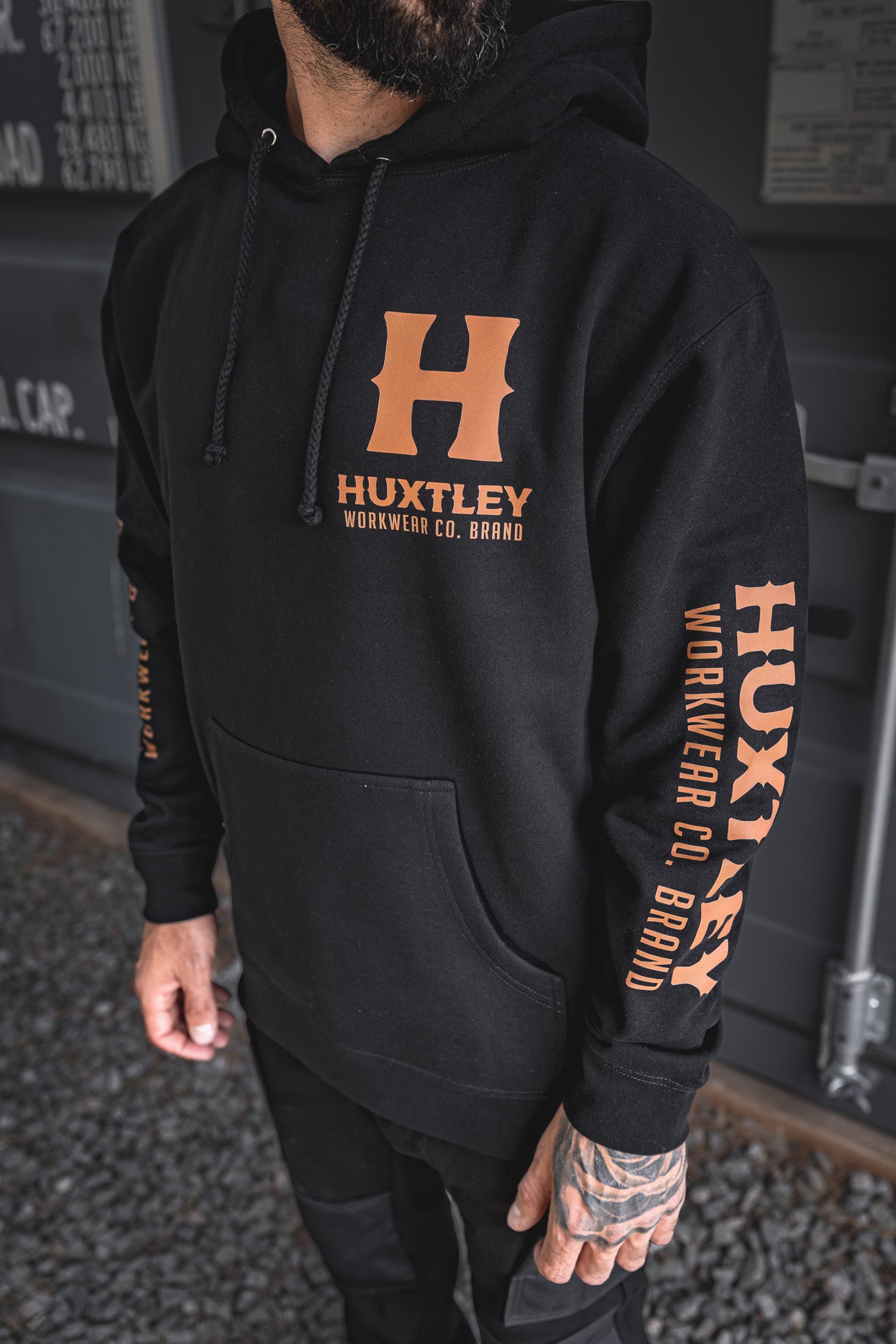 
                  
                    Detailed shot of the Full Print Hoodie’s front and sleeve, featuring bold orange Huxtley Workwear Co. Brand prints on black cotton. Built tough for the jobsite, styled for the street.
                  
                
