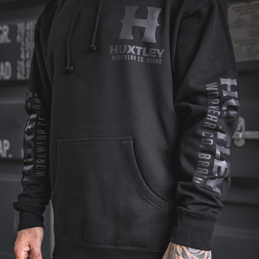 
                  
                    Front view of the Huxtley Full Print Hoodie with sleek black-on-black logo print. Minimalist design, heavyweight feel, and clean tonal branding down the sleeves.
                  
                