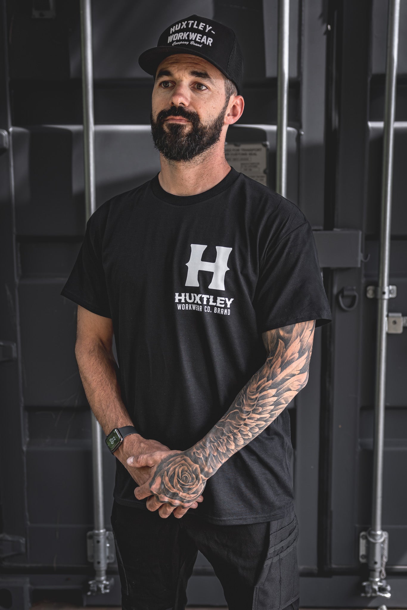 
                  
                    Model wearing the Huxtley Full Print tee in classic black, featuring a bold white front logo. Built for grit and clean looks.
                  
                