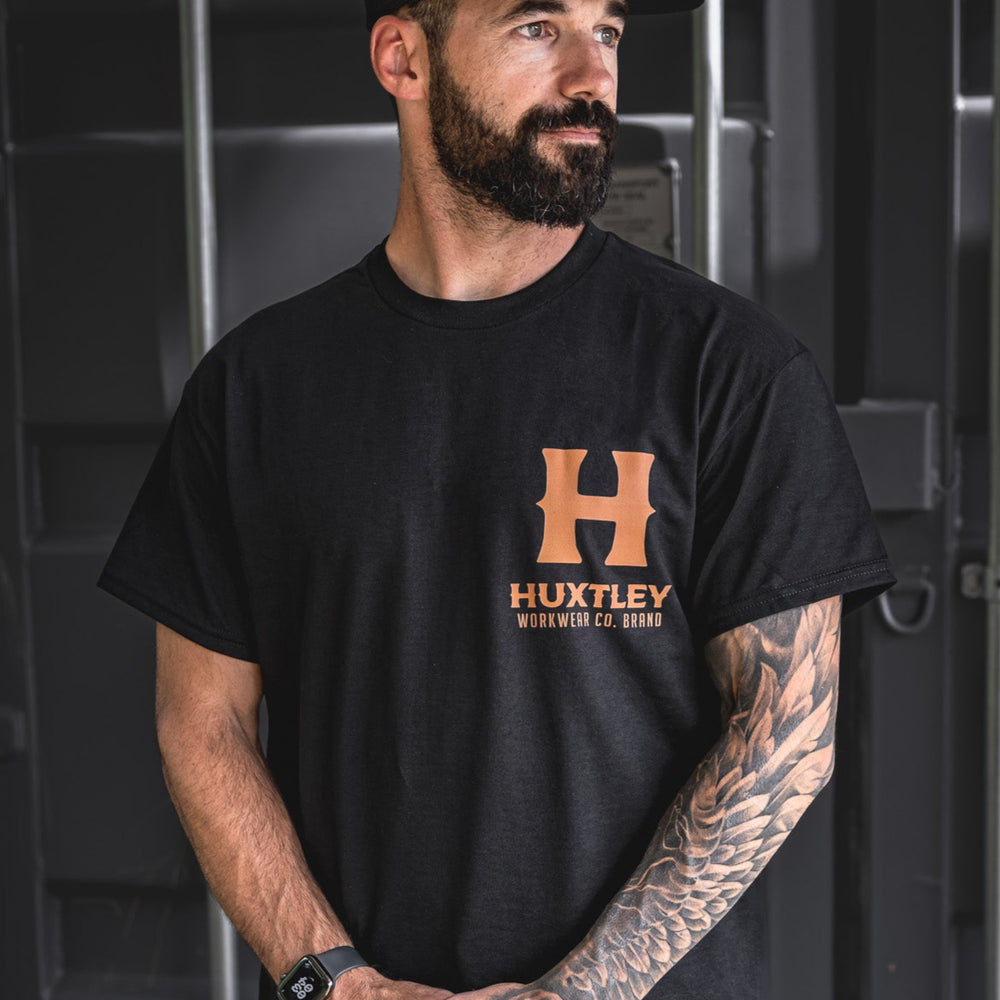 
                  
                    Front view of the Huxtley Full Print t-shirt featuring the whiskey-colored logo on black. Classic workwear fit with bold branding.
                  
                