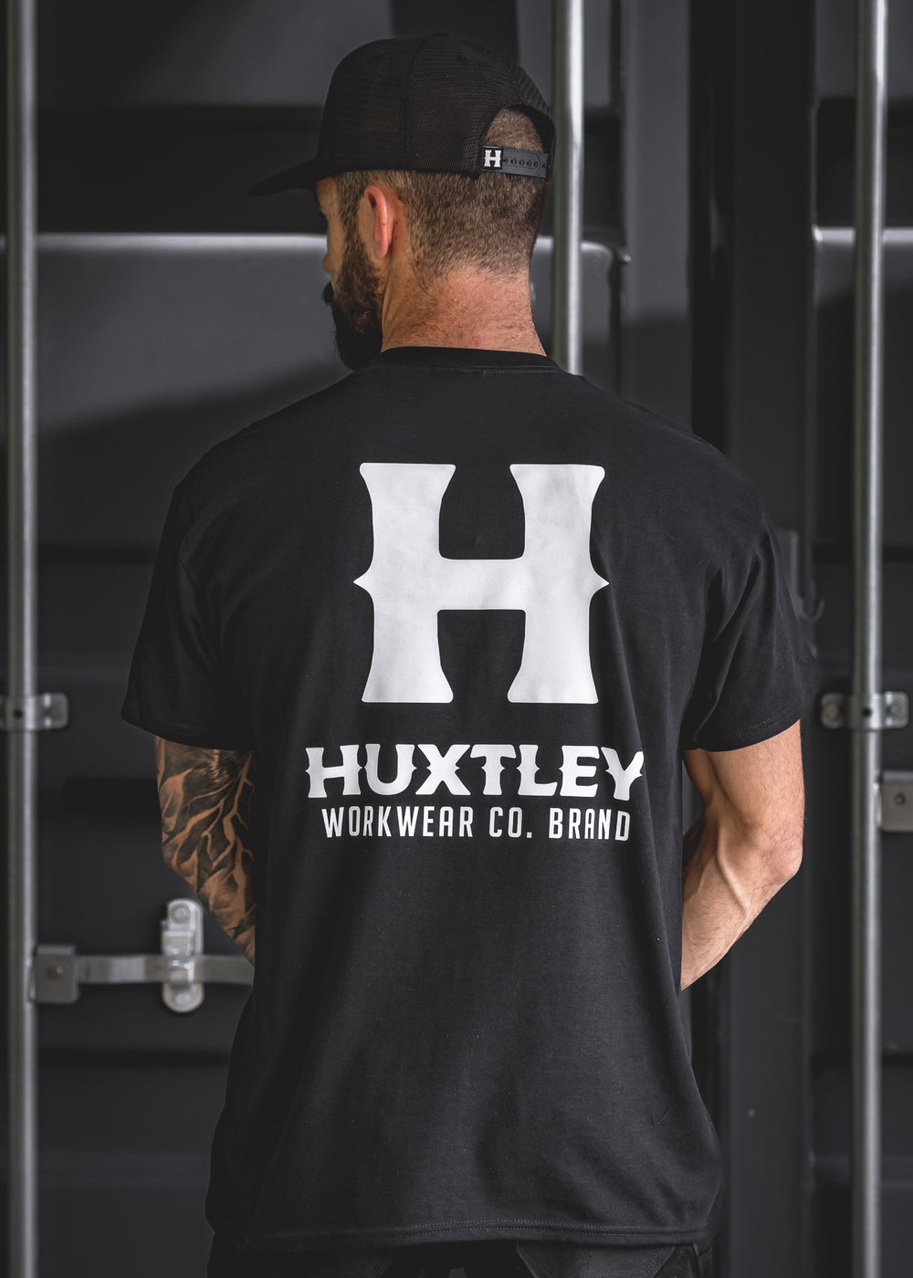 Rear view of the Huxtley Full Print t-shirt showcasing the bold white logo print on black cotton. Rugged streetwear made for the jobsite.