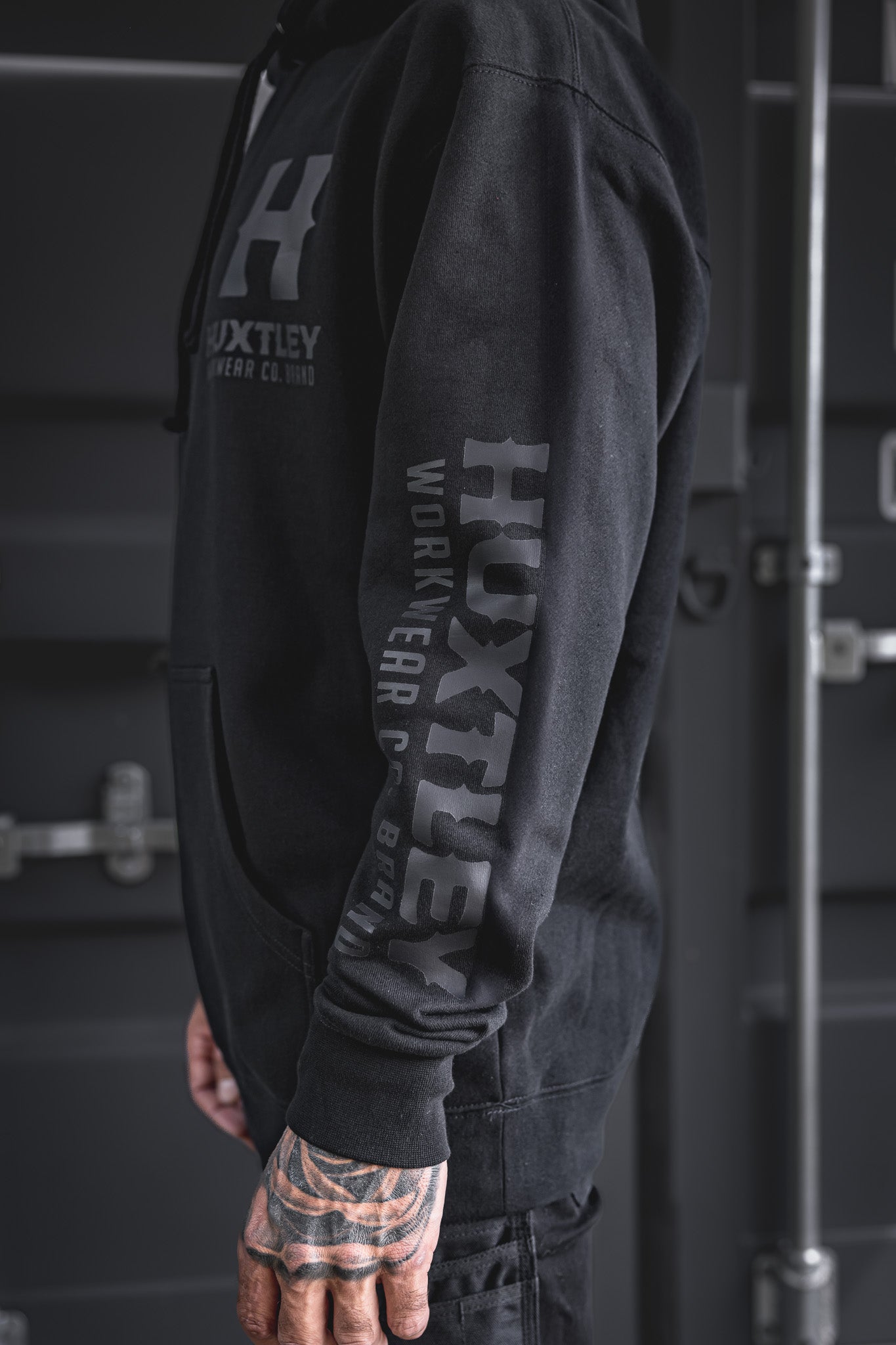 
                  
                    Detailed side view of the Huxtley Full Print Hoodie featuring tonal black-on-black logo on sleeve and chest. A clean, low-key look with industrial edge.
                  
                