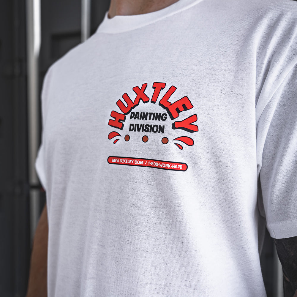 
                  
                    Close-up of the Huxtley Painting Division graphic on a crisp white work tee. Bold red and black print stamped across the chest, complete with the hotline and website for the real ones who paint and hustle hard.
                  
                