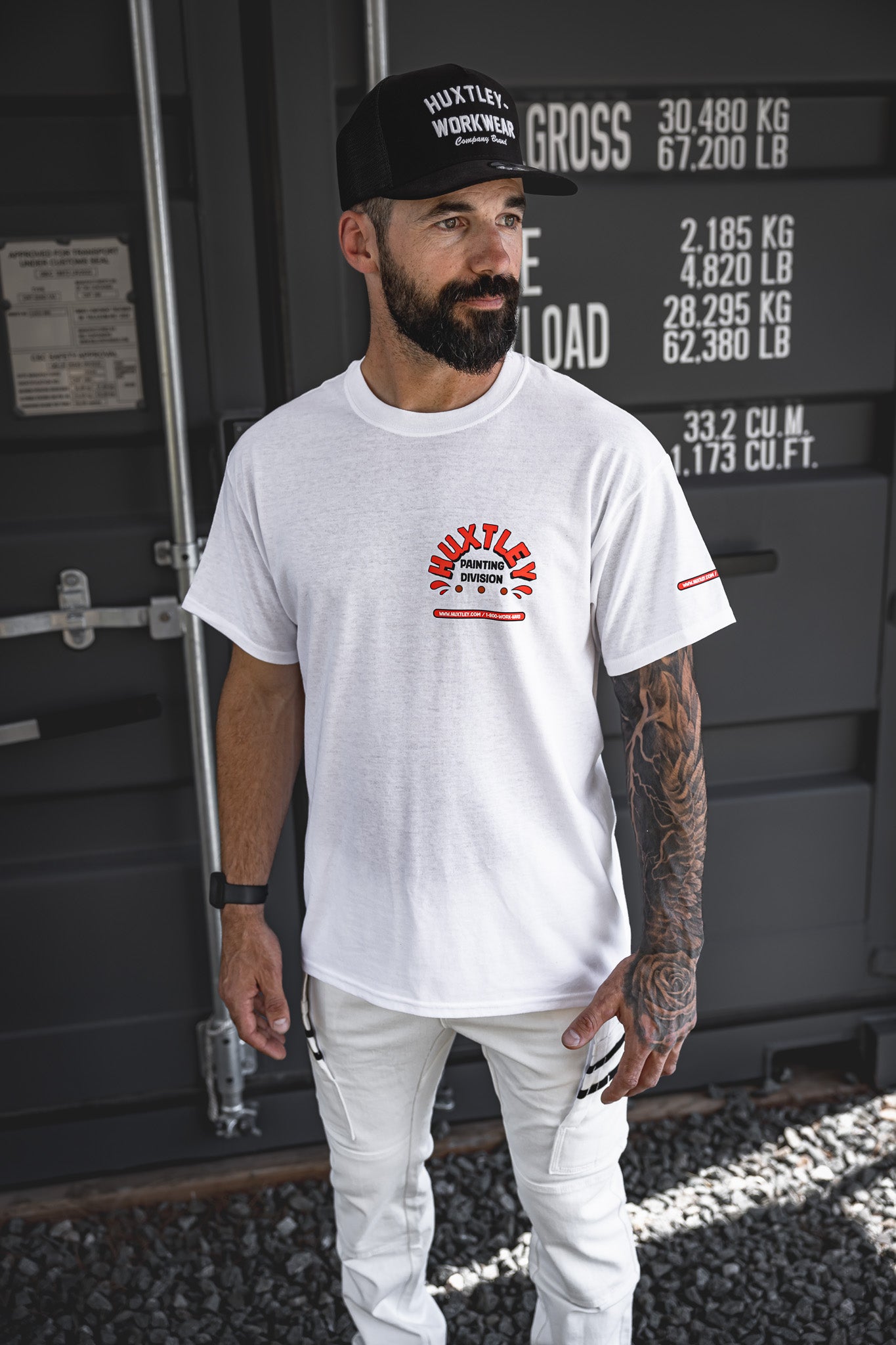 
                  
                    Full-body shot of the Huxtley Painting Division tee styled with white painter pants and a classic Huxtley Throwback snapback. The front chest print pops against the clean white tee, made for pros who keep it tight and roll it right.
                  
                