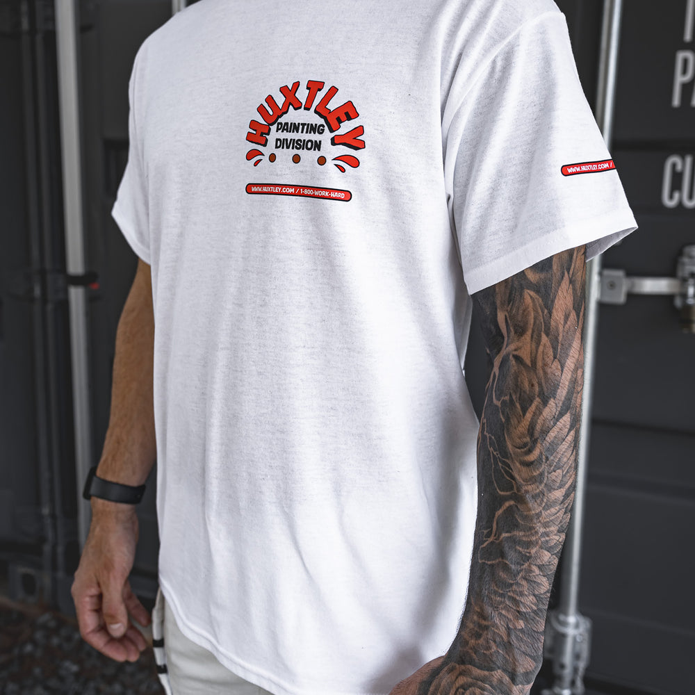 
                  
                    Side angle of the Huxtley Painting Division white tee, showing the bold chest print and sleeve logo hit. Worn by a tatted tradesman rocking Huxtley white Work Pants and grit-ready style—made for those who paint it tight and roll it right.
                  
                
