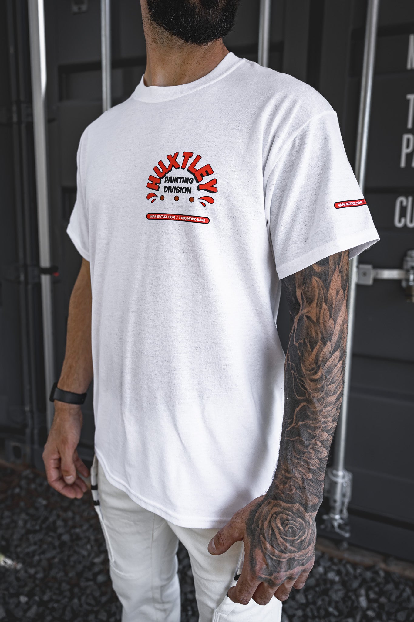 
                  
                    Side angle of the Huxtley Painting Division white tee, showing the bold chest print and sleeve logo hit. Worn by a tatted tradesman rocking Huxtley white Work Pants and grit-ready style—made for those who paint it tight and roll it right.
                  
                