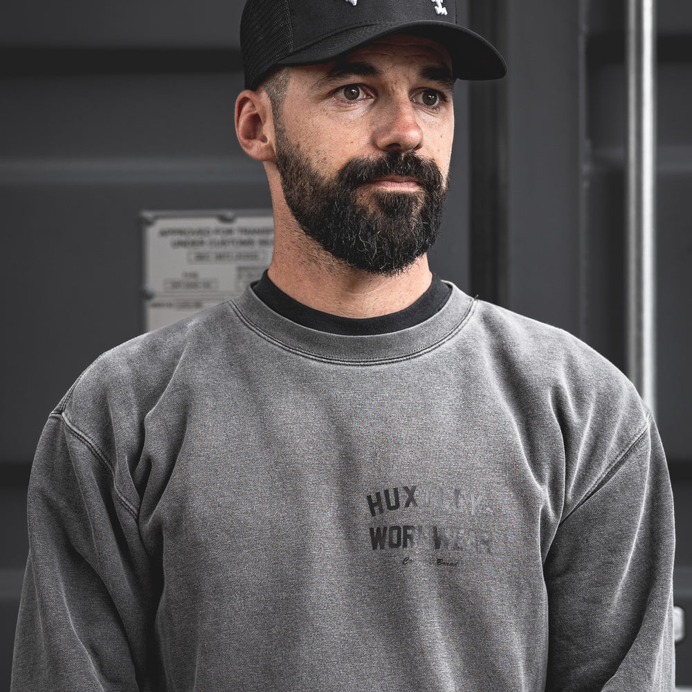 
                  
                    Reverse Logo Huxtley cap shown on model in workwear setting. Curved white embroidery arches boldly across the crown, blending grit and style in true jobsite fashion.
                  
                