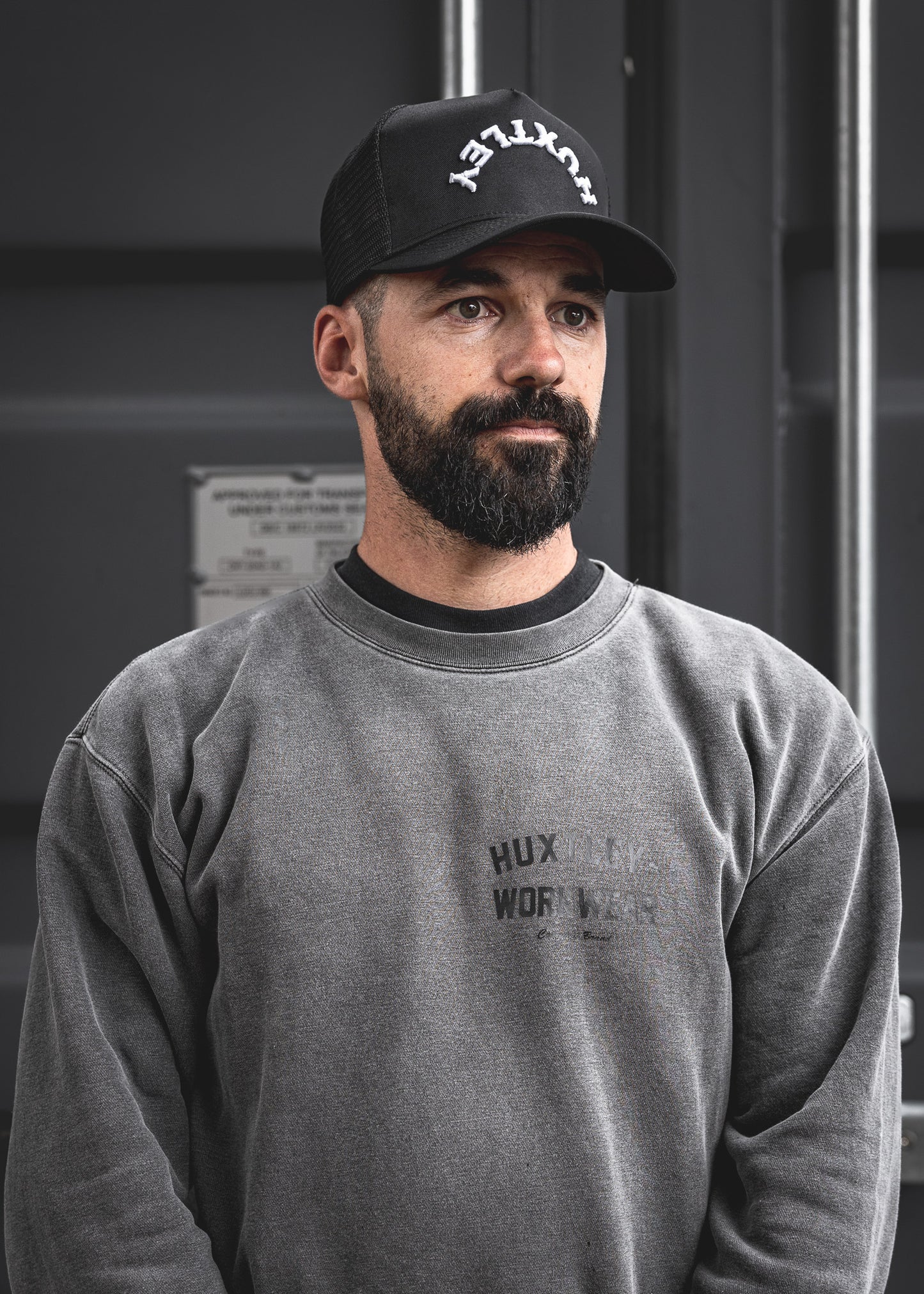 
                  
                    Reverse Logo Huxtley cap shown on model in workwear setting. Curved white embroidery arches boldly across the crown, blending grit and style in true jobsite fashion.
                  
                