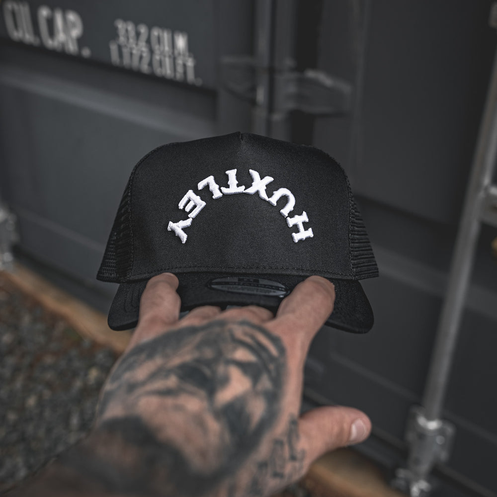 
                  
                    Close-up of the Huxtley Reverse Logo cap in hand. Bold white arched embroidery, structured front, and breathable mesh — made for the grind, built for everyday wear.
                  
                