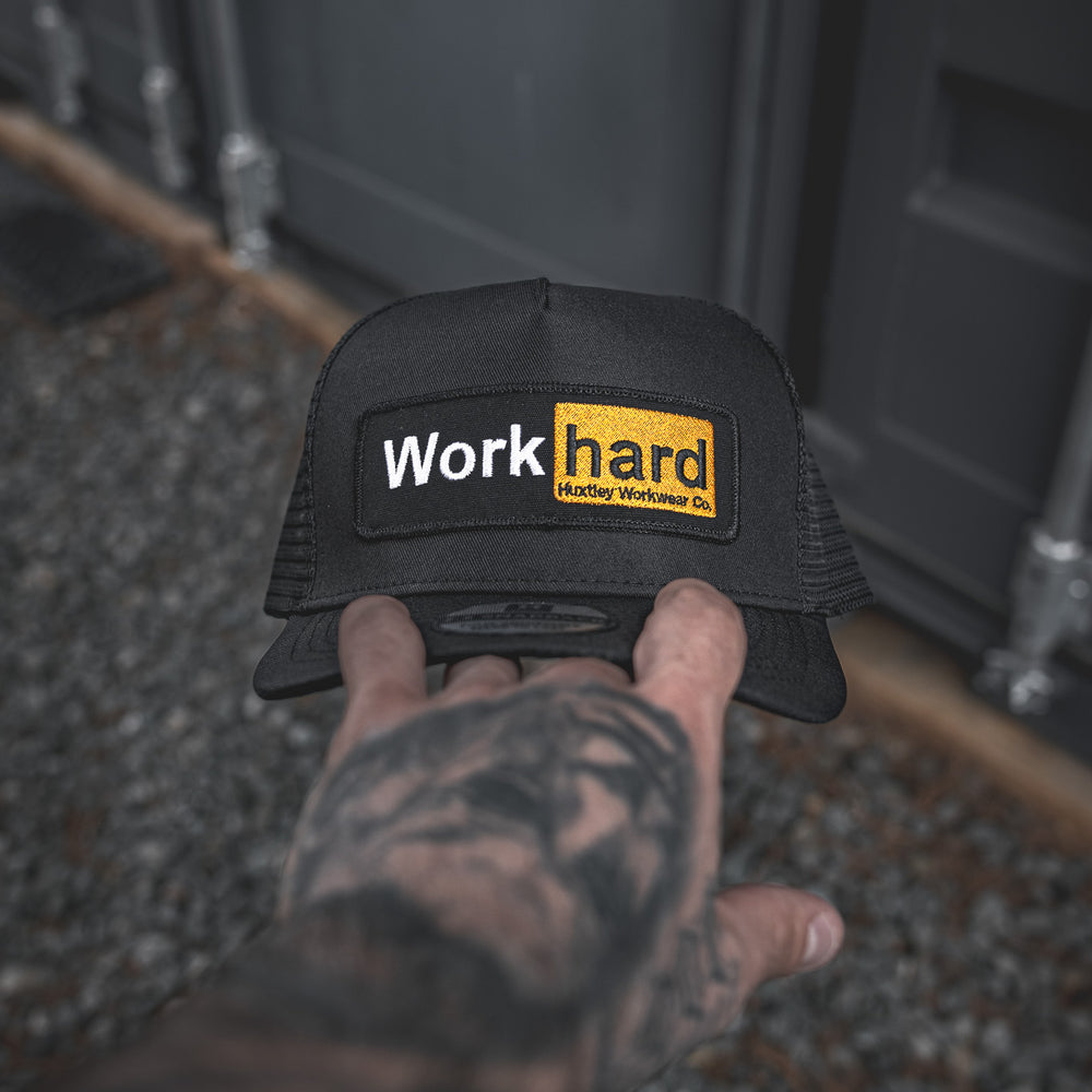 
                  
                    Hand-held view of the Huxtley trucker cap featuring the bold “Work hard” patch. Built tough, worn proud.
                  
                