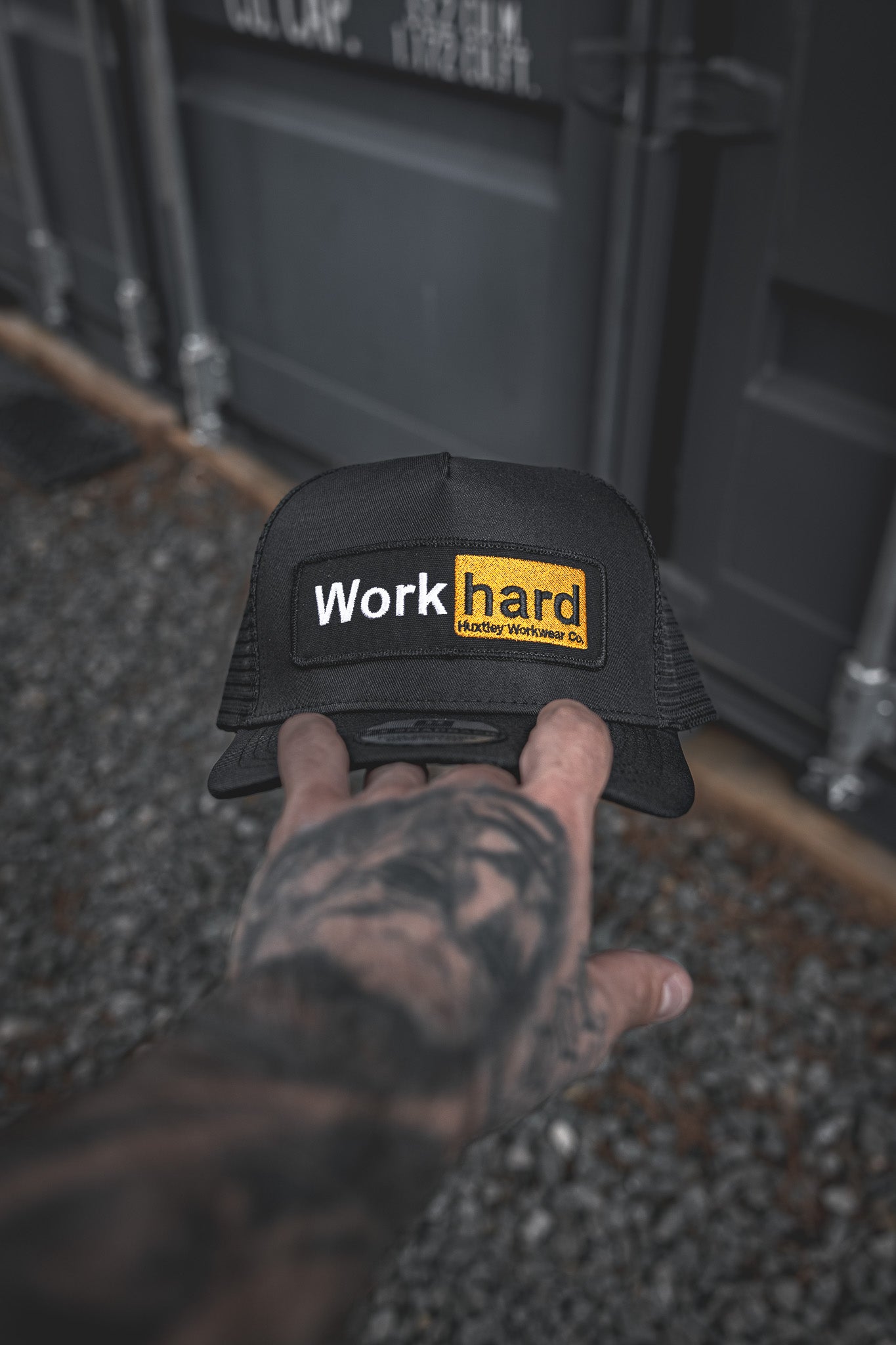 
                  
                    Hand-held view of the Huxtley trucker cap featuring the bold “Work hard” patch. Built tough, worn proud.
                  
                