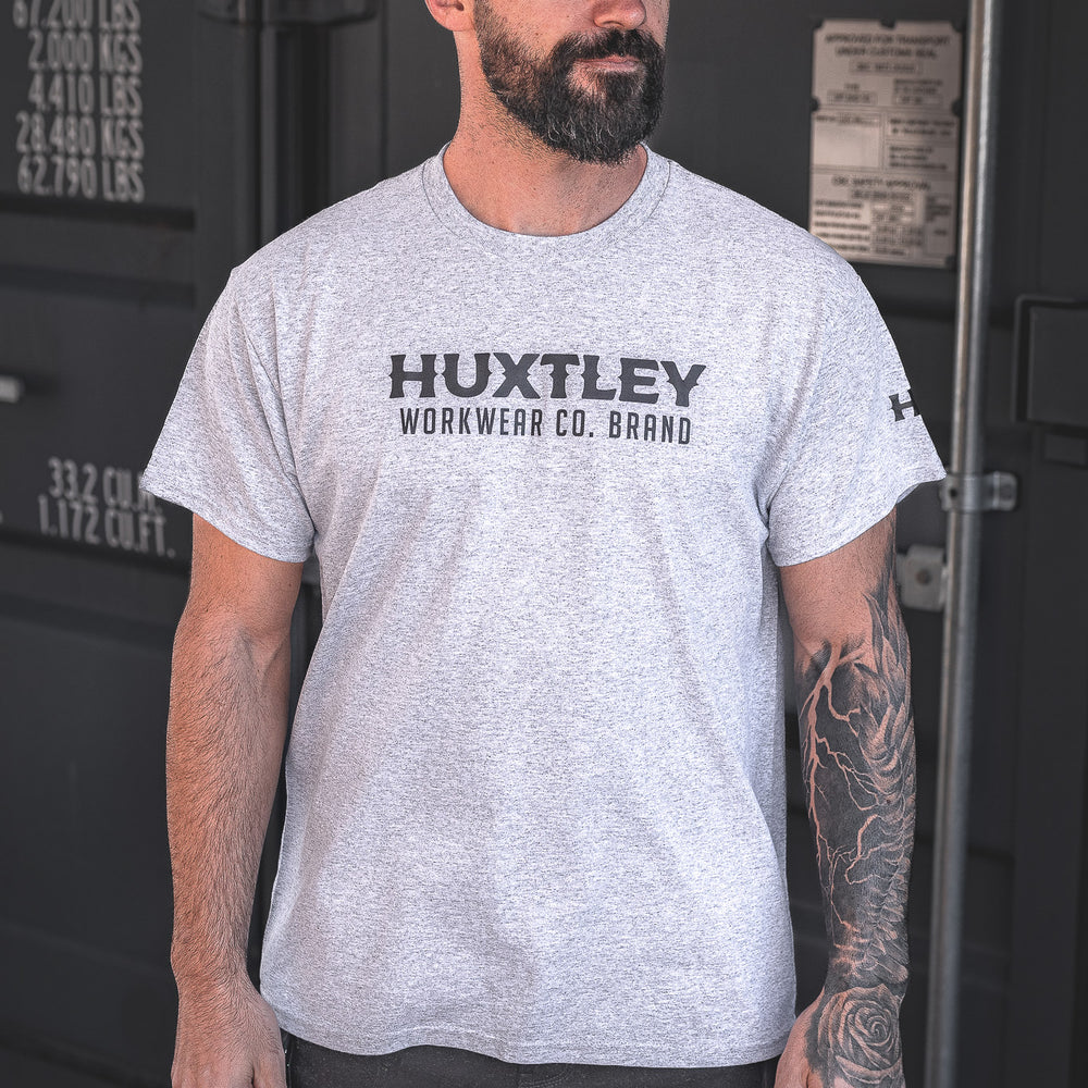 
                  
                    The Huxtley Workwear Co. Brand tee in heather grey, worn by a model on site. Comfortable fit, bold chest logo, and durable enough for long days on the job.
                  
                