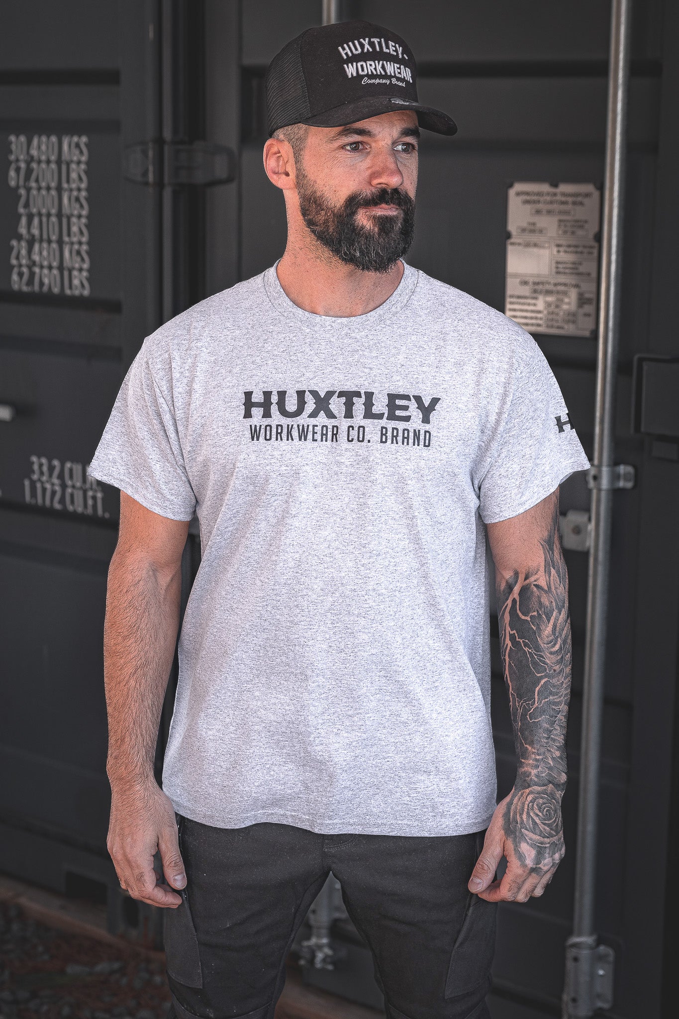 
                  
                    The Huxtley Workwear Co. Brand tee in heather grey, worn by a model on site. Comfortable fit, bold chest logo, and durable enough for long days on the job.
                  
                